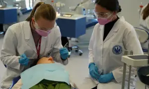 Studentki stomatologii ćwiczą na fantomie. W białych fartuchach, rękawiczkach i okularach ochronnych, z precyzją wykonują zabieg.