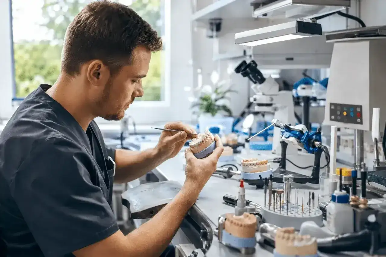 Pracownia protetyczna. Technik dentystyczny pracuje nad modelem szczęki, co wpływa na jego zarobki.