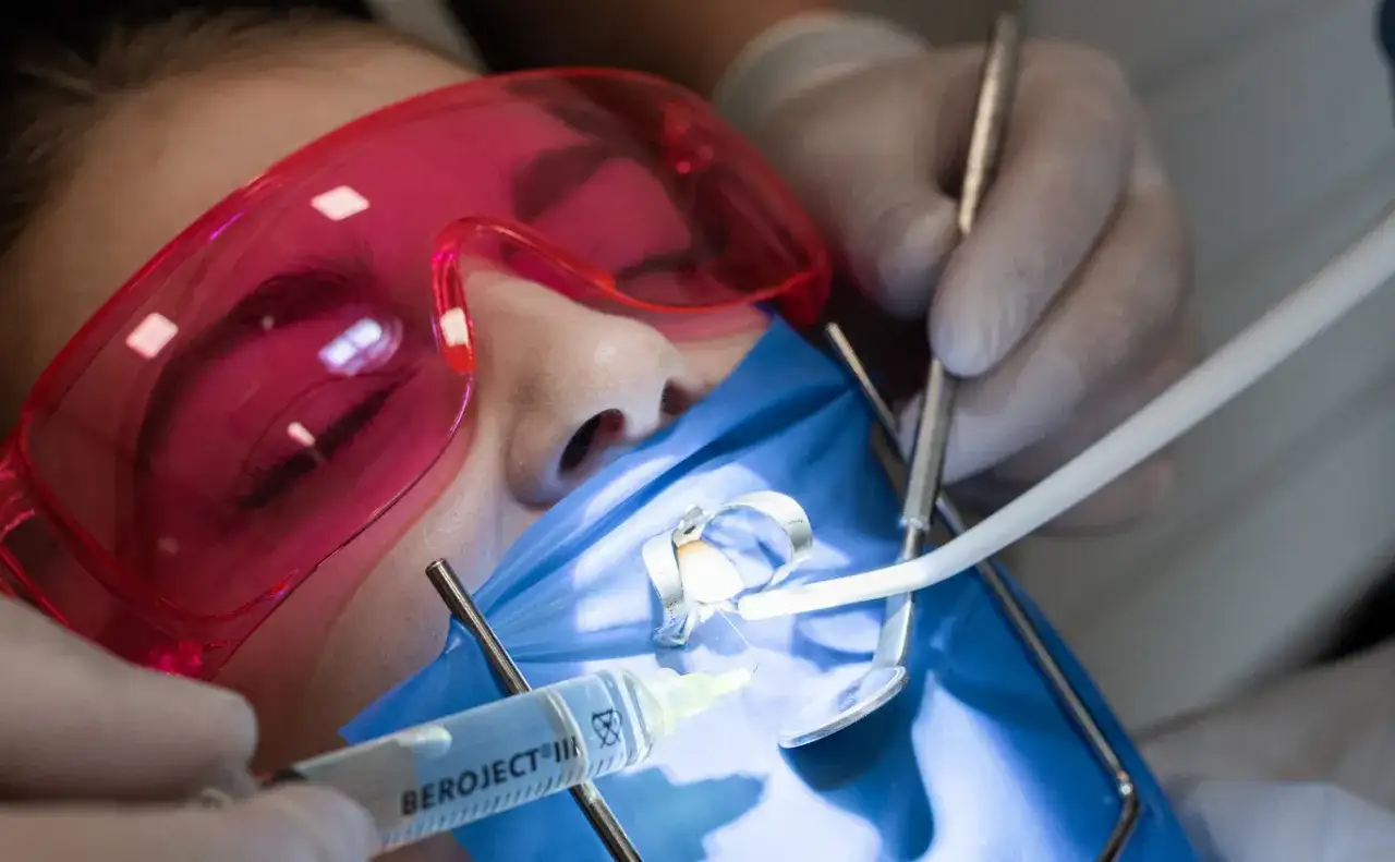 Precyzyjne leczenie kanałowe pod mikroskopem. Dentysta używa narzędzi i strzykawki do wykonania zabiegu.