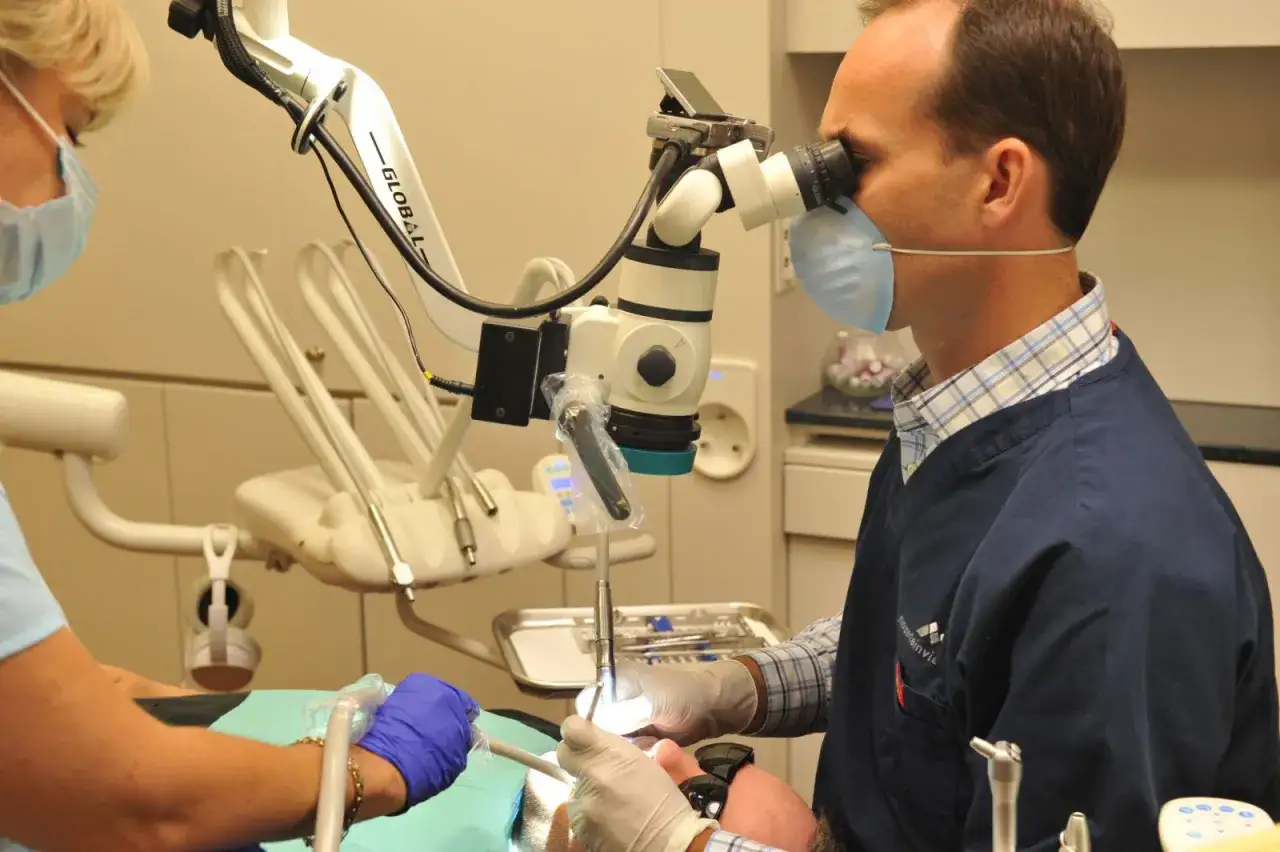 Dentysta wykonuje leczenie kanałowe pod mikroskopem, precyzyjnie pracując przy użyciu specjalistycznego sprzętu.