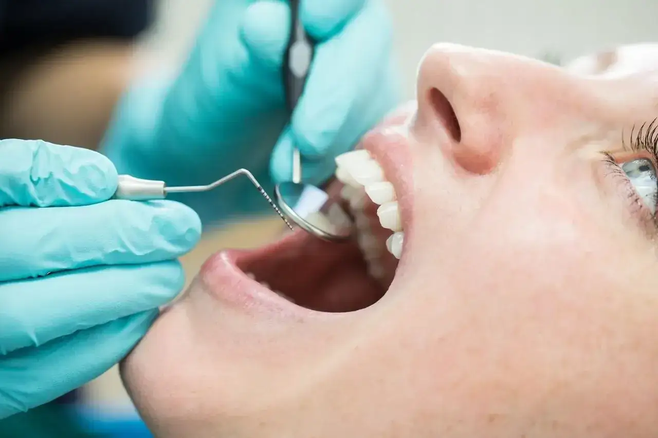 Dentysta bada zęby pacjentki. Zastanawiasz się nad lakierowaniem zębów? Cena zabiegu może być niższa niż myślisz.