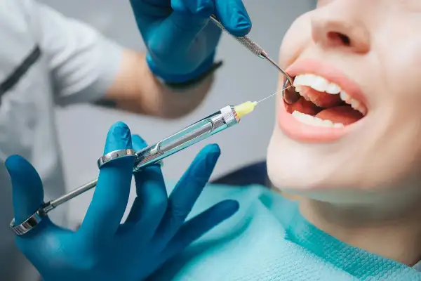 Znieczulenie u dentysty. Pacjent czuje ból szczęki po znieczuleniu zęba, gdy lekarz przygotowuje się do zabiegu.